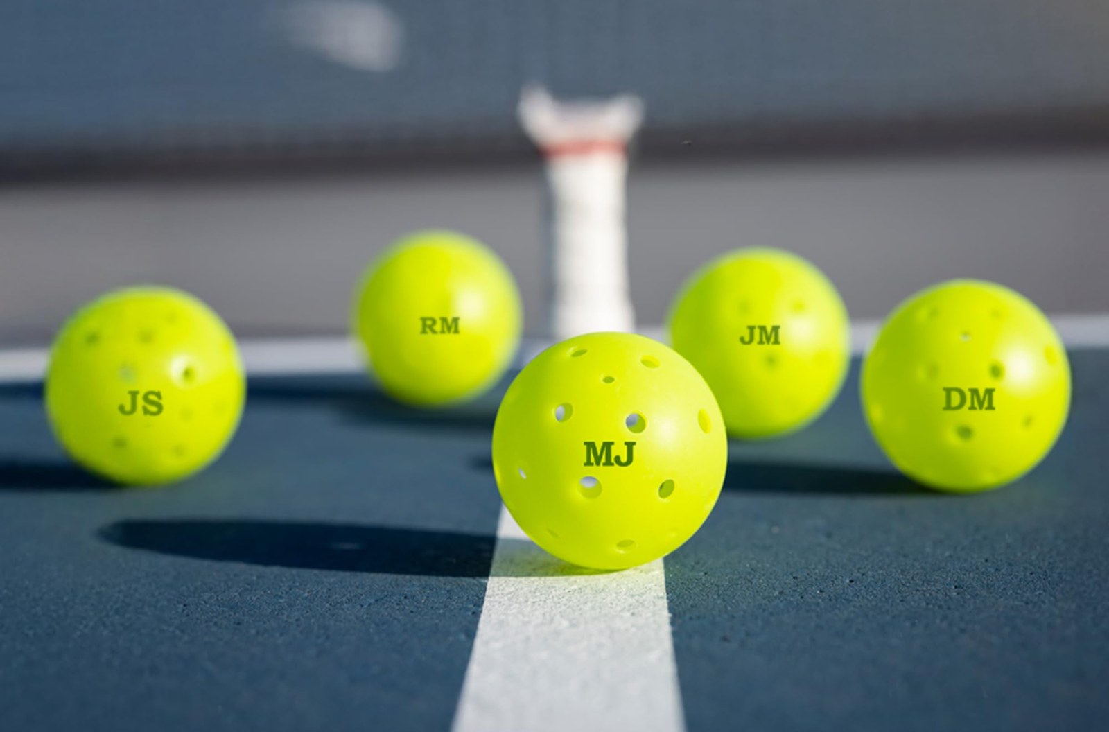 Pickleballs stamped with initials on a court