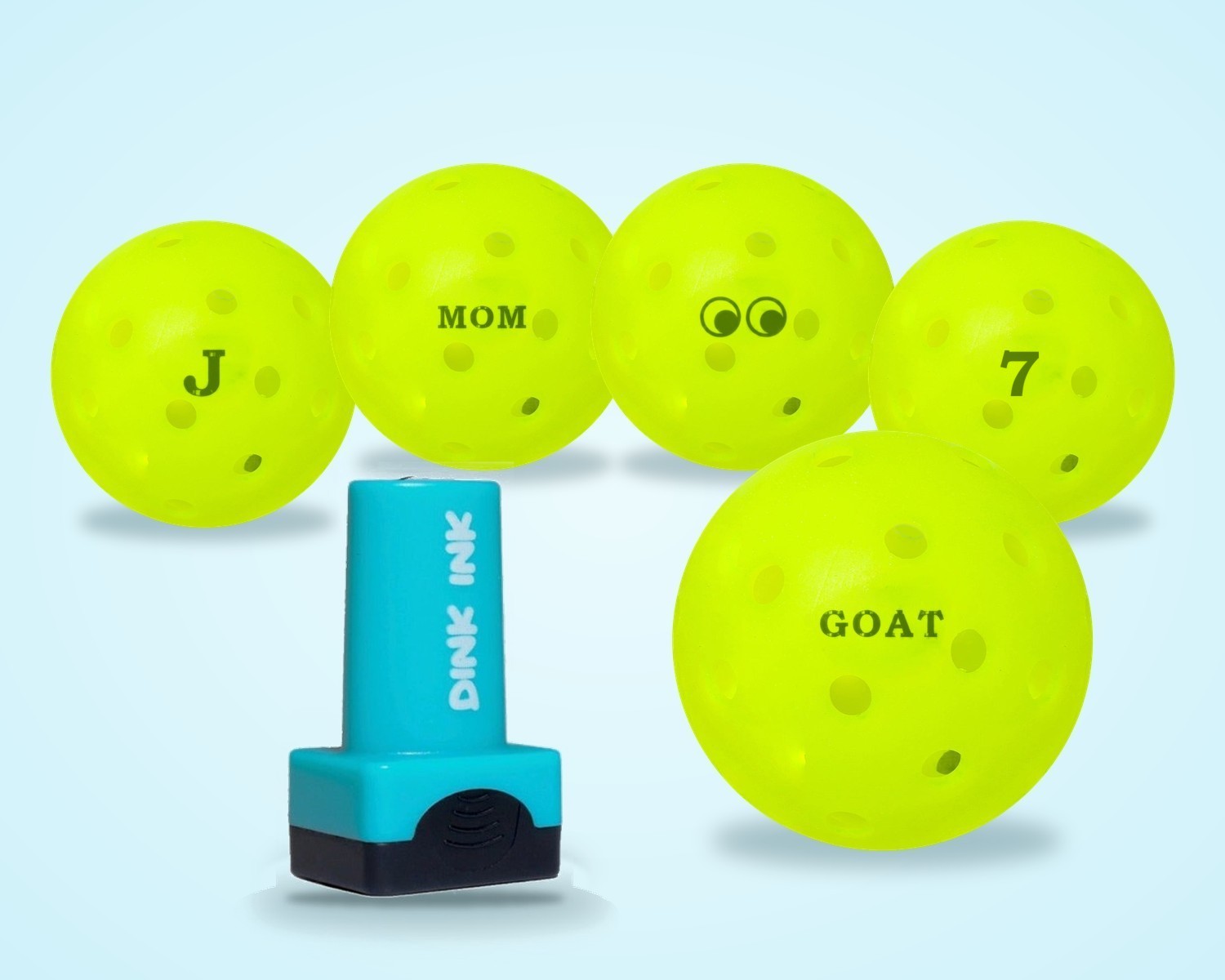 The Dink Ink stamper in front of pickleballs stamped J, MOM, a side-eyes design, 7 and GOAT