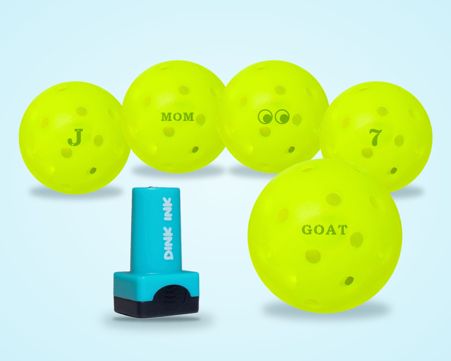 The Dink Ink stamper in front of pickleballs stamped J, MOM, a side-eyes design, 7 and GOAT