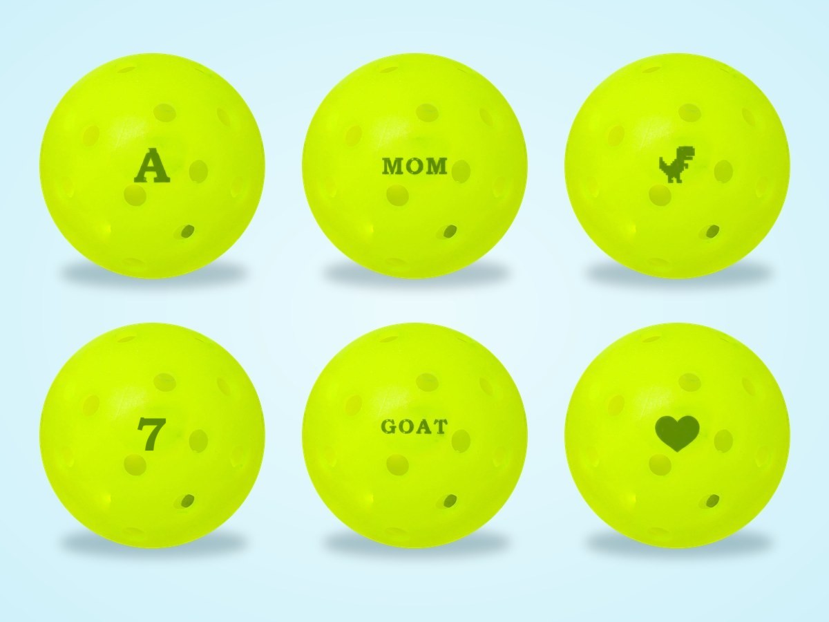 Six pickleballs stamped A, MOM, a dinosaur, 7, GOAT and a heart